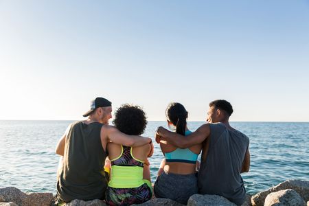 Back view of two young sporty couples hugging while resting after work out outdoorsの写真素材