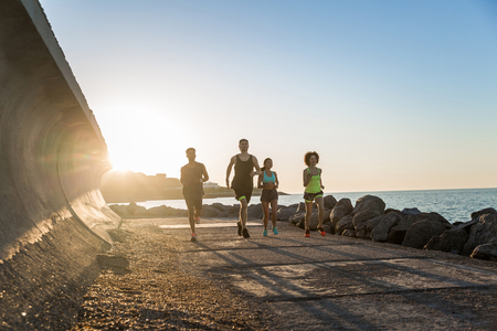 Group of young sporty friends jogging together outdoors at the beachの写真素材