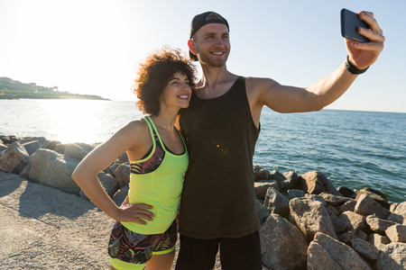 Happy smiling fitness couple in sportswear taking a selfie while standing together outdoorsの写真素材
