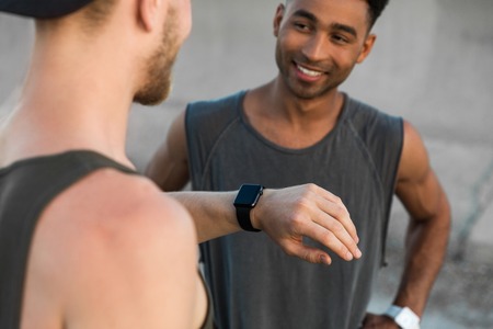 Two young men resting after running workout and checking fitness app on smart watch outdoorsの写真素材