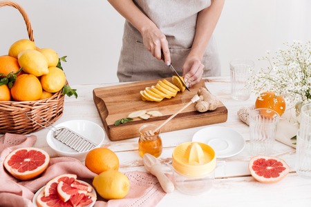 Cropped picture of young woman standing indoors near table with a lot of citruses and cut the lemon.の写真素材