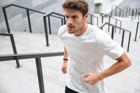 Close up of a healthy male runner in sport clothes running upstairs at the stadium