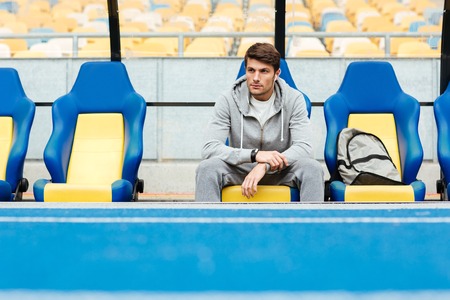 Young male athlete in sportswear sitting on a stadium seats and waiting for his coachの写真素材