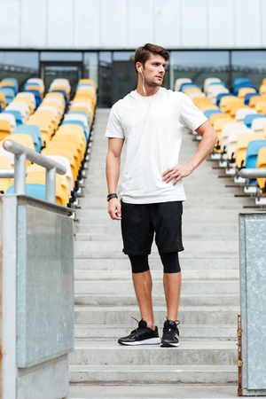 Picture of handsome young sports man at the stadium outdoors listening music and looking aside.の写真素材