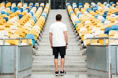 Back view image of young sports man standing at the stadium outdoors and looking aside.の写真素材