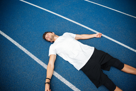 Tired male athlete resting after running while lying on a racetrack at the stadiumの写真素材