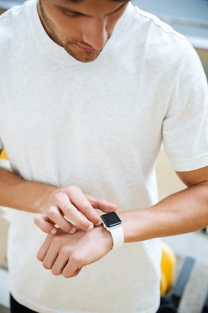 Picture of concentrated young sports man looking at watch at the stadium outdoors.の写真素材