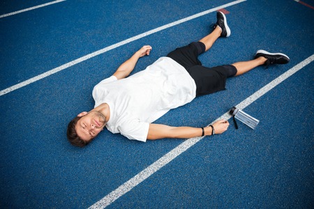Tired young sportsman lying on a racetrack with bottle of water at the stadiumの写真素材