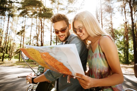 Image of young happy loving couple holding map outdoors near scooter. Looking aside.の写真素材