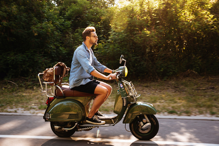 Image of serious young bearded man on scooter outdoors. Looking aside.の写真素材