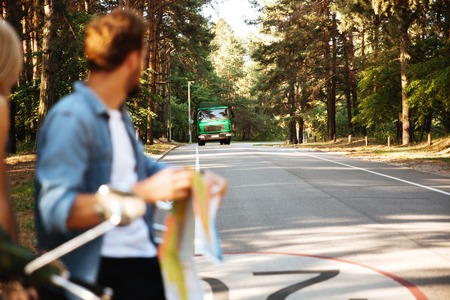 Picture of young happy loving couple holding map outdoors near scooter looking at car.