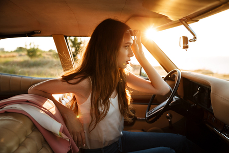 Young pretty woman in sunglasses sitting in a retro car and looking at front view mirrorの写真素材