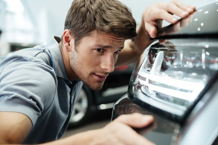 Young male customer examining and looking carefully at a new car at a dealership