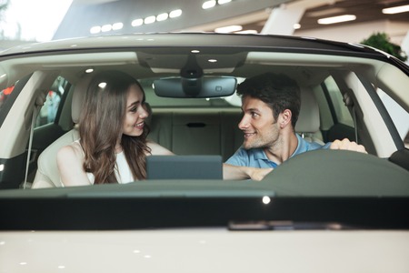 Smiling excited couple sitting inside a new car at the dealership