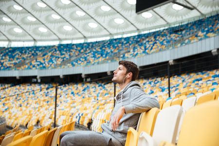 Photo of handsome young sports man at the stadium outdoors listening music and looking aside.の写真素材