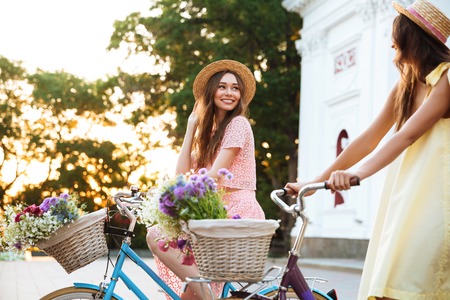 Two happy smiling women in hats riding vintage bicycles on a city streetの写真素材