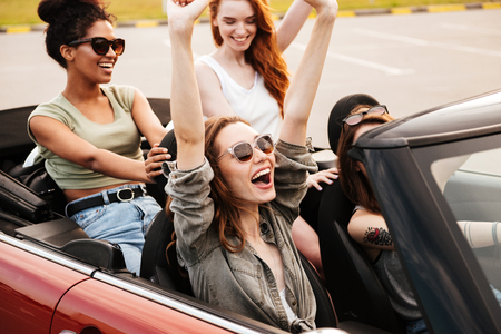 Picture of happy emotional four young women friends sitting in car outdoors.の写真素材