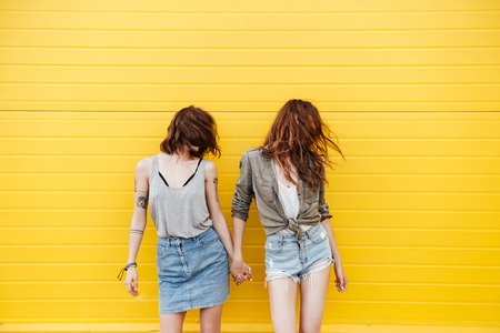 Picture of two young smiling women friends standing over yellow wall shaking hair.の写真素材