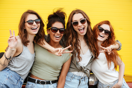 Image of four young happy women friends standing over yellow wall. Looking at camera.の写真素材