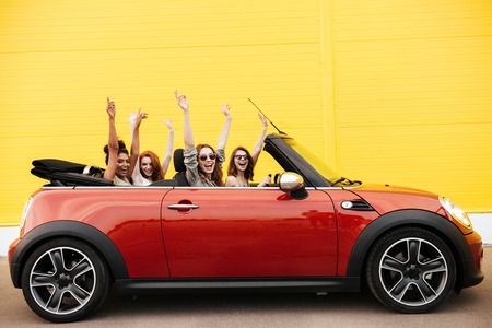 Image of happy emotional four young women friends sitting in car outdoors. Looking camera.の写真素材