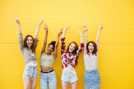 Picture of young smiling women friends standing over yellow wall. Looking at camera.の写真素材