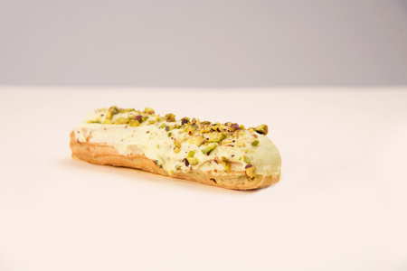 Close up of eclair with white cream and nuts isolated over white