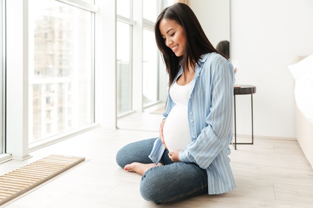Image of happy young pregnant woman sitting at home indoors looking aside.の写真素材
