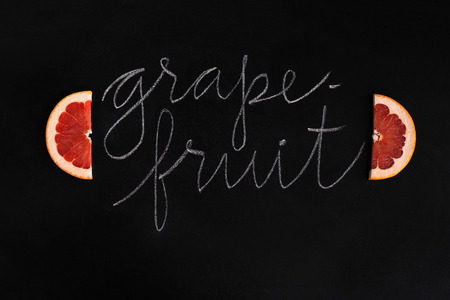 Fresh sliced grapefruit with the inscription over black backgroundの写真素材