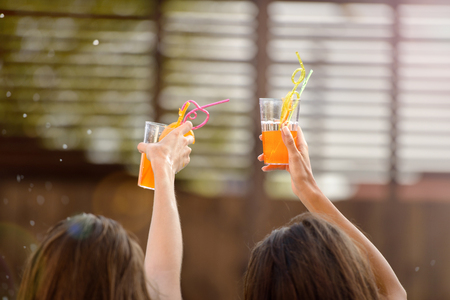 Back view cropped image of two young woman celebrating and toasting with cocktail glasses outdoorsの写真素材