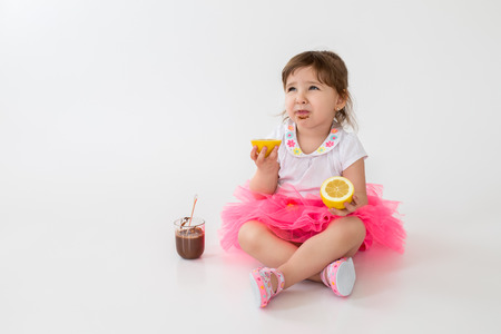 Photo of little children girl sitting over white background. Looking aside while eating chocolate dessert with lemon.の写真素材