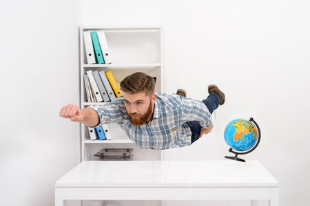 Concentrated bearded man in plaid shirt flying above office desk like supermanの写真素材
