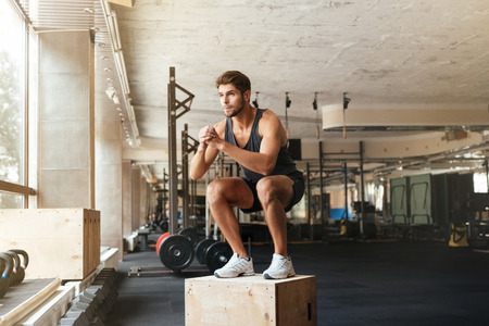 Portrait of male athlete standing on box in gym. crouchesの写真素材