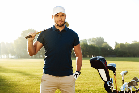 Handsome confident male golfer standing with golf club on a green fieldの写真素材
