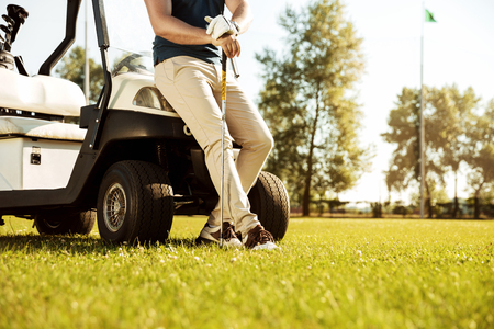 Cropped image of a male golfer leaning on a cart and holding golf club outdoorsの写真素材