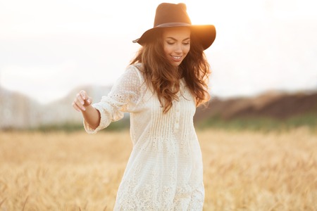 Happy smiling woman with long hair in hat walking at the wheat fieldの写真素材