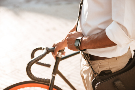 Cropped picture of young african handsome man early morning with bicycle walking outdoors.の写真素材