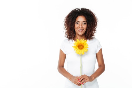 Image of cheerful young african woman standing isolated over white background. Looking camera holding flower.の写真素材
