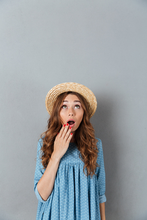 Image of shocked young pretty woman standing over grey wall wearing hat. Looking aside.の写真素材