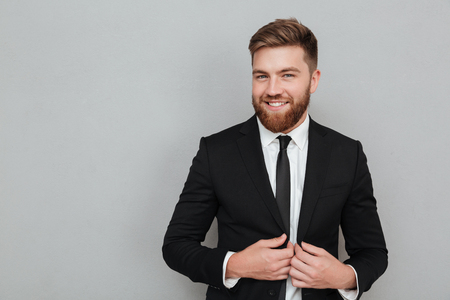 Smiling handsome businessman in suit standing and laughing isolated over gray backgroundの写真素材