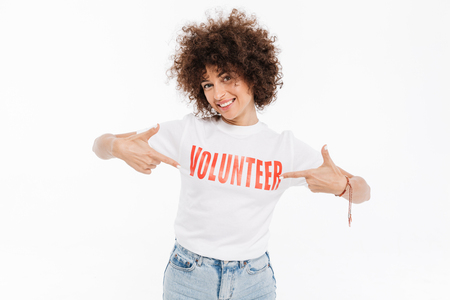 Smiling casual woman pointing two fingers at volunteer t-shirt isolated over white backgroundの写真素材