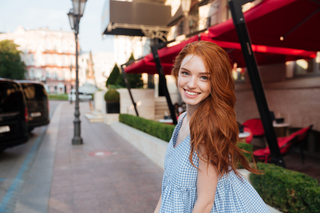 Smiling redhead girl standing outside on a city street and looking at cameraの写真素材