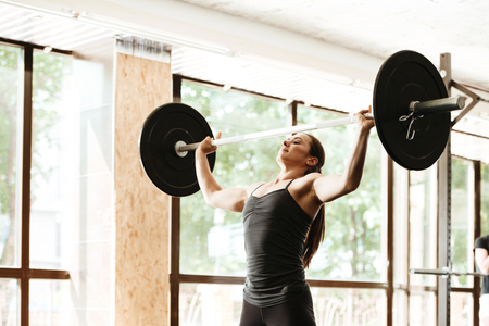 Strong young woman working out with a barbell at the gymの写真素材