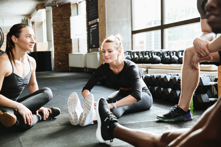 Photo of group of sports strong people sitting in gym. Looking aside talking with each other.の写真素材