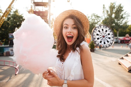 Close up portrait of a smiling excited girl holding cotton candy at amusement parkの写真素材