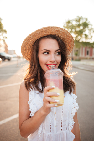 Picture of beautiful young woman outdoors drinking juice. Looking aside.の写真素材