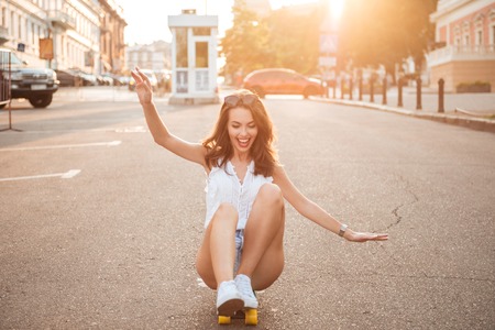 Image of smiling young woman on skateboard outdoors. Looking aside.の写真素材