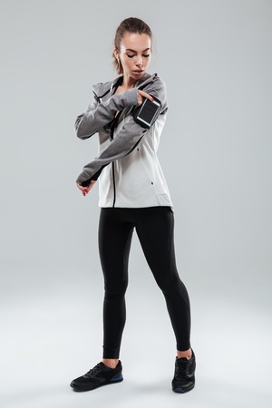 Full length image of a sports woman using smartphone on armband over gray backgroundの写真素材