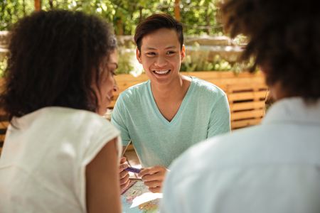 Smiling asian sitting by the table outdoor with his friendsの写真素材