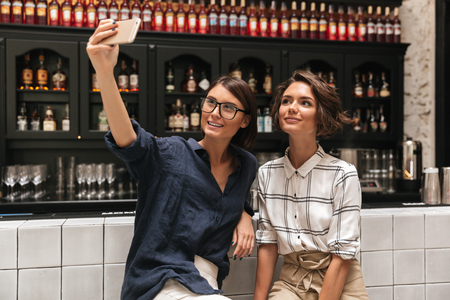 Two pretty smiling women making selfie on smartphoneの写真素材
