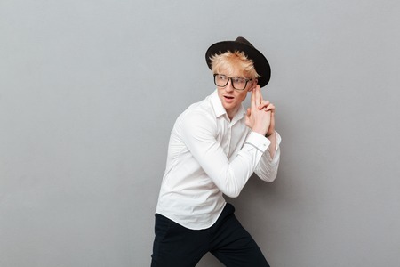 Photo of handsome cheerful young caucasian man wearing glasses standing isolated over grey wall near...